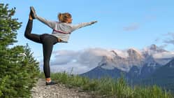 Junge Frau macht eine Yoga-Pose auf einem Bergweg