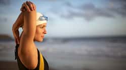Eine Schwimmerin im Badeanzug stretcht sich am Strand
