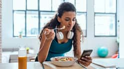 Junge Frau isst einen Salat und schaut auf ihr Handy