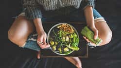 Eine Frau isst vegane Salat Bowl mit einem grünen Smoothie