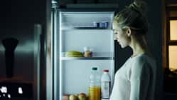 Eine Frau steht nachts vor dem Kühlschrank und schaut, was sie essen möchte