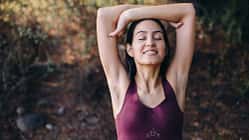 Eine Frau in Sport-Bh verschränkt die Arme über dem Kopf