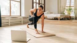 Eine Frau praktiziert Yoga auf einer Matte vor einem Laptop