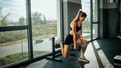 Determined sportswoman performing bulgarian split squats with dumbbells in a gym