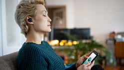 Eine Frau mit geschlossenen Augen die ein Smartphone in der Hand hält 