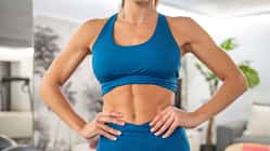 Eine trainierte Frau in blauer Sportkleidung zeigt ihre trainierten Bauchmuskeln