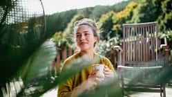 Woman with morning cup of coffee, sitting on patio and enjoying moment for herself. Portrait of beautiful woman.