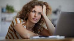 Frau mit lockigen Haaren sitzt nachdenklich vor einem Laptop und stützt den Kopf in die Hand