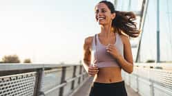 Sportliche Frau joggt lächelnd über eine Brücke