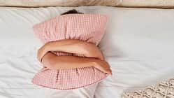 Eine Frau liegt im Bett und verbirgt ihr Gesicht hinter einem Kissen, das sie mit beiden Armen umschlungen hält