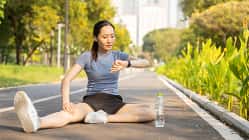 Eine Frau sitzt auf der Straße und stretcht sich in Sportkleidung während sie auf ihre Fitnessuhr schaut