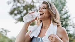 Eine ältere Frau trinkt Wasser nach dem Training mit einem Handtuch über der Schulter