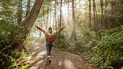 Frau läuft im Wald durch eine Waldlichtung und streckt die Arme zu den Seiten aus