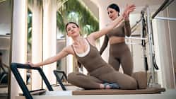 Eine Pilates-Trainerin unterstützt eine Frau beim Pilates-Training auf einer Reformer-Maschine