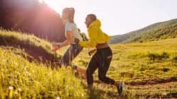 Zwei Freuen joggen durch eine hügelige Landschaft und werden von der Abendsonne angeschienen