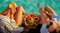 Zwei Frauen sitzen am Pool und essen einen Obstteller