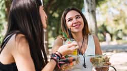 Zwei junge Frauen sitzen im Park und essen Salat