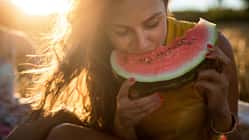 Eine junge Frau sitzt in der Sonne und isst eine Wassermelone.