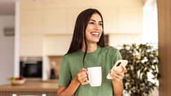 Eine jungeFrau genießt lächelnd ihren Kaffee und hält ihr Handy in der anderen Hand