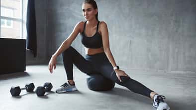 Frau stretcht ihr Bein und hat Hanteln und einen Fitnessball dabei