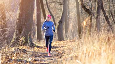 Joggerin läuft in langem Sportoutfit durch einen herbstlichen Wald