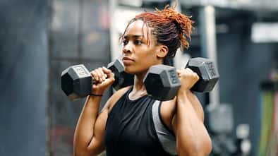 Eine durchtraininerte Frau traininert mit zwei Hanteln in einem Fitnessstudio.