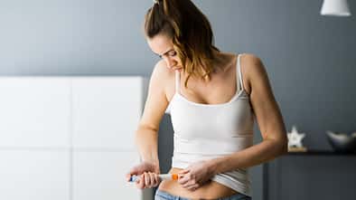 Junge Frau spritzt sich Medikament in den Bauch.
