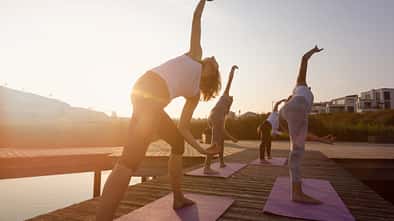group of women exercising yoga on jetty in the city at sunrise