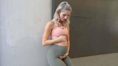 Kaya Renz schaut in Sportkleidung auf ihren Babybauch und berührt diesen