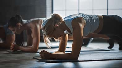mehrere Frauen führen auf Yogamatten den Unterarmstütz aus