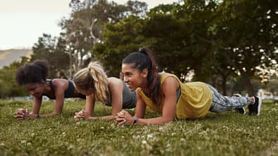 Drei Frauen machen Planks im Park.