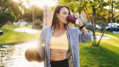 sportliche Frau in Sportkleidung mit Yogamatte trinkt Kaffee