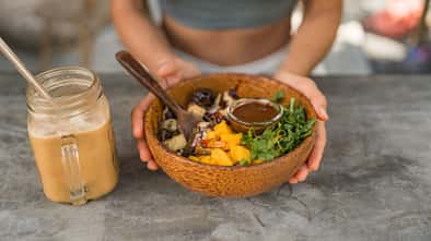 Eine Frau sitzt am Tisch mit einer veganen Salatbowl 