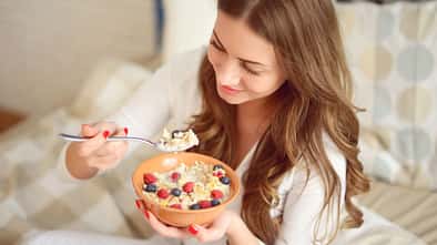 Frau im Schlafanzug isst Müsli mit Beeren