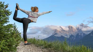 Junge Frau macht eine Yoga-Pose auf einem Bergweg