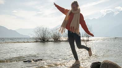 Frau hüpft von Stein zu Stein am See