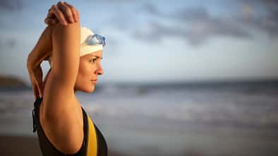 Eine Schwimmerin im Badeanzug stretcht sich am Strand