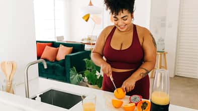 Frau in Sportkleidung bereitet Smoothie zu und schneidet Obst