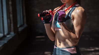 Closeup sporty young fit woman fitness bra pants gloves sportswear hold skipping jumping rope around neck have break rest training cardio exercise workout gym healthy lifestyle concept copy space