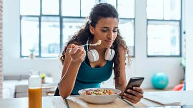 Junge Frau isst einen Salat und schaut auf ihr Handy