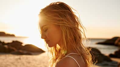 Eine Frau mit blonden Haaren am Strand bei Sonnenuntergang