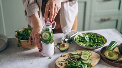 Eine Frau macht grünes Gemüse in einen Mixer