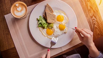 Eine Frau schneidet 3 Spiegeleier auf einem Teller