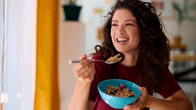 Eine Frau isst lachend ein gesundes Müsli aus einer blauen Schale 