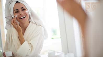 Eine Frau im Bademantel mit Turban cremt sich ihr Gesicht ein Eine Frau im Bademantel mit Turban cremt sich ihr Gesicht ein