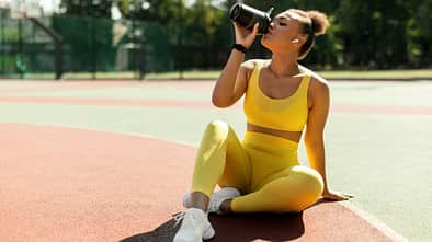Eine Frau in gelber Sportkleidung trinkt aus einem Shaker 