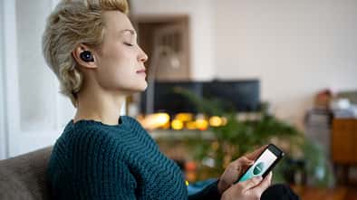 Eine Frau mit geschlossenen Augen die ein Smartphone in der Hand hält 