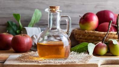 Karaffe mit Apfelessig und Äpfeln im Hintergrund