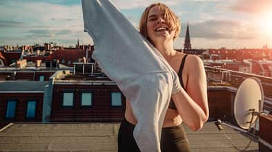 Portrait of smiling woman wearing t-shirt on rooftop against dramatic sky