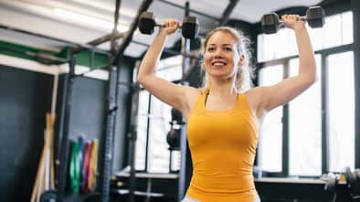 Eine Frau im gelben Oberteil macht Übungen mit Kurzhanteln für die Arme